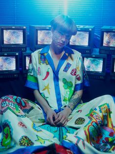 a man sitting on top of a bed covered in lots of tv monitors behind him