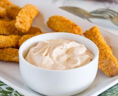 a white plate topped with tater tots covered in ranch dip next to fried chicken strips