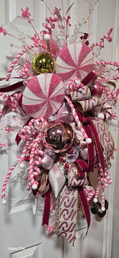 a pink and white christmas wreath with candy canes, bells and decorations on the front door