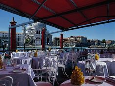 an outdoor dining area with tables and chairs under a red awning over the water