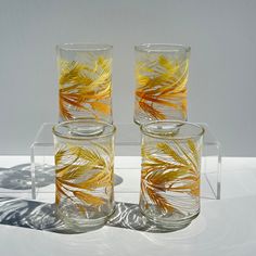 three clear glass vases with yellow and orange leaves on the inside are sitting on a white surface