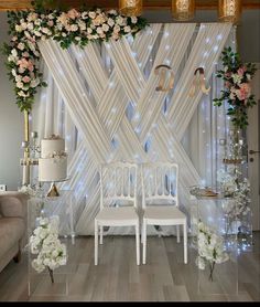 two white chairs sitting next to each other in front of a wall with flowers on it