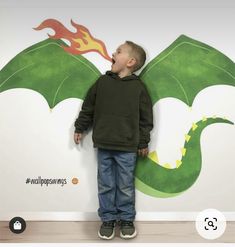 a little boy standing in front of a wall with a dragon on it's back