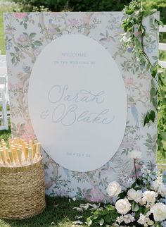 a welcome sign with flowers and candles in front of it on the grass next to a basket