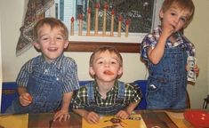 three young boys sitting at a table with food in front of them and one boy eating an apple