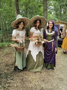 three women dressed in period clothing standing next to each other on a dirt road with trees behind them