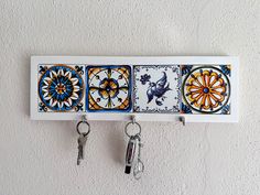 three keys are hanging on the wall next to two hooks with decorative tiles painted on them