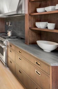 a modern kitchen with stainless steel appliances and wooden cabinets, along with white dishes on shelves