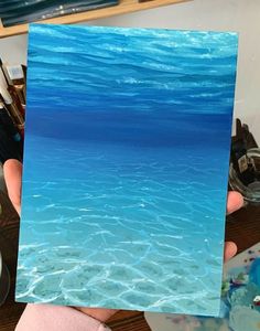 a person holding up a piece of art that looks like the ocean in blue water