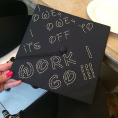 a black graduation cap with white letters and numbers on the front is held up by a woman's hand