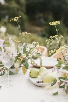 the table is set with white plates and flowers in vases, pears and apples