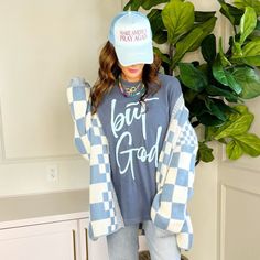 a woman standing in front of a plant wearing a blue and white sweater with the words got good written on it