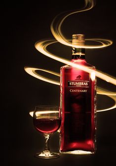 a bottle of wine next to a glass filled with red liquid and light streaks in the background