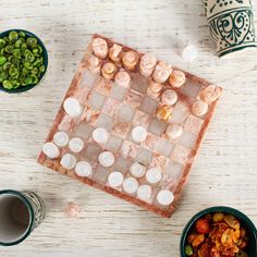 a marble chess board surrounded by bowls of peas and other foods on a white wooden table