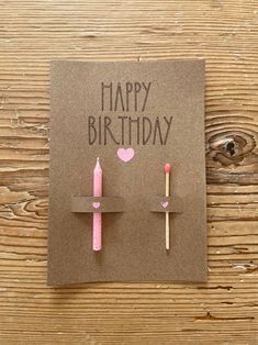 a birthday card with two matches and a heart on the top, sitting on a wooden table