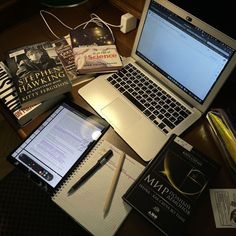 an open laptop computer sitting on top of a wooden desk next to books and magazines