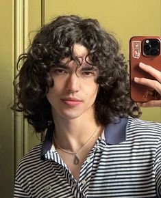 a man with curly hair taking a selfie in front of a mirror while wearing a striped shirt