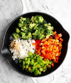 broccoli, onions, and carrots in a skillet on a marble counter