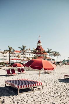 red and white striped lounge chairs on the beach with an umbrella in front of a hotel