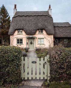 a white house with a thatched roof and green hedges around it's front door