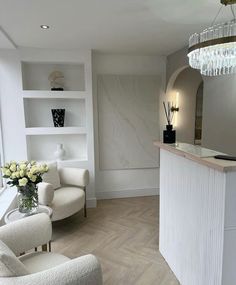 a room with white furniture and flowers in the vases on the counter, along with two chairs