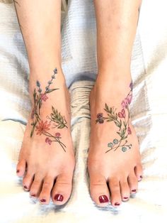 two feet with flower tattoos on them sitting on top of a white bed next to each other