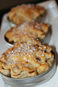 three pies sitting on top of a white table next to each other in metal tins