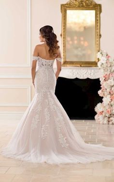 a woman in a wedding dress looking at the back of her gown, with flowers on the wall