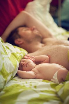 a black and white photo of a baby sleeping on someone's back in bed