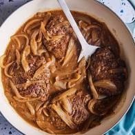 a bowl filled with meat and noodles on top of a blue cloth next to a spoon