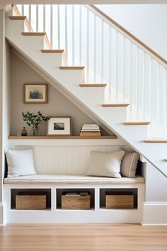 a white bench under the stairs with baskets underneath it and some pictures on the wall