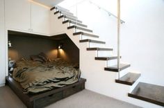 there is a bed under the stairs in this room, and it looks very neat