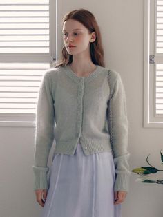 a woman standing in front of a window wearing a sweater and skirt