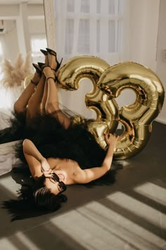 a woman laying on the floor next to a giant gold number balloon in front of her