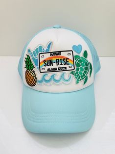 Light blue and white trendy trucker hat with iron on patches- "Hawaii Sun-Rise aloha state" in the middle with hang loose, pineapple, turtle & waves. This adorable beachy style hat would be a great gift for a friend. This adult size hat was handmade by myself. The hat is made of fabric & foam with mesh along the back. It is easily adjustable in the back & has a ponytail holder. It is comfortable, lightweight & flexible. It fits the average adult size head, measuring about 8" diameter inside the hat.  Spot clean only. I don't recommend washing items with iron on patches because it'll weaken the adhesive glue under the patches.  Feel free to message me with any questions or if you would like to request a custom hat. any questions or if you would like to request a custom hat. Fun Blue Trucker Hat For Vacation, Fun Summer Trucker Hat With Embroidered Patch, Fun Summer Snapback Hat With Patches, White Patches Hat For Summer, Casual Summer Trucker Hat With Embroidered Patch, Fun Summer Baseball Cap With Patches, Casual Snapback Hat With Embroidered Patch For Summer, Casual Summer Baseball Cap With Patches, Casual Baseball Cap With Patches For Summer