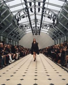 a model walks down the runway in front of a large group of people wearing black