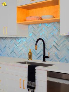 a kitchen with white cabinets and blue glass tile backsplash, gold trimmings