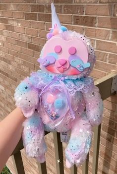 a pink and blue teddy bear sitting on top of a wooden fence