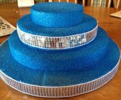 three tiered blue cake sitting on top of a wooden table next to a remote control