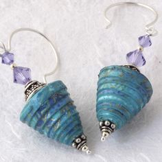 two sea shells are hanging from silver earwires on a white surface with purple crystal beads