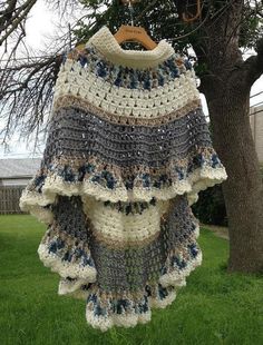 a crocheted sweater hanging from a tree in front of a house on the grass