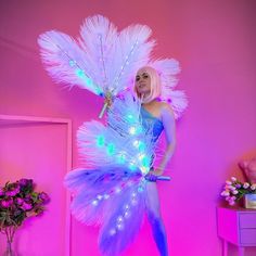 a woman is dressed up as a fairy with lights on her body and feathers around her legs