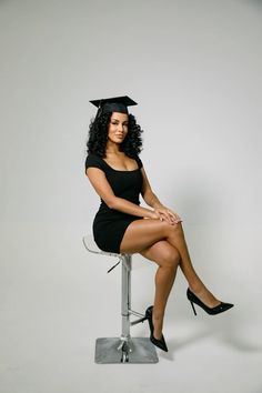 a woman sitting on top of a stool wearing a black graduation cap and gown with her legs crossed