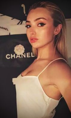 a woman with blonde hair wearing a white top and posing for the camera in front of a chanel sign