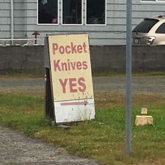 a sign that says pocket knives yes in front of a house with a car behind it