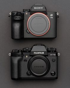 two cameras sitting next to each other on top of a gray surface with the same lens