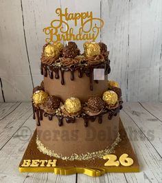 a birthday cake with chocolate icing and gold decorations on top is sitting on a wooden table