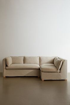 a beige couch sitting on top of a wooden floor next to a white wall in an empty room