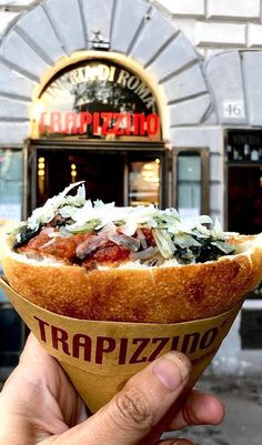 a hand holding up a half eaten hot dog in front of a pizza restaurant sign