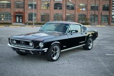 an old mustang sitting in a parking lot next to a brick building with large windows